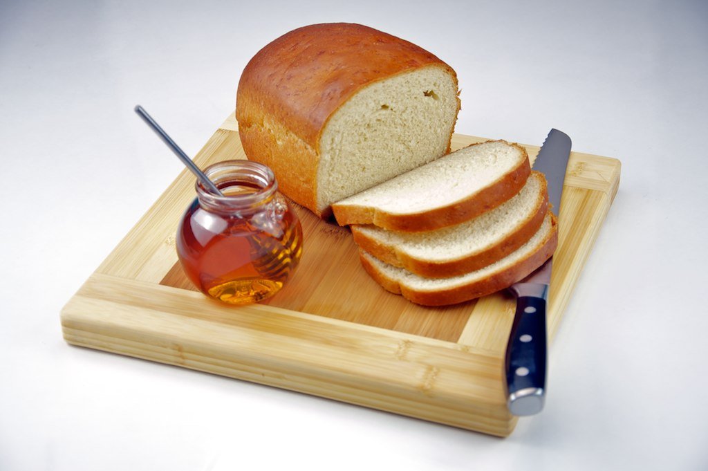 Tarro de miel con una cuchara de madera junto a un pan casero recién cortado